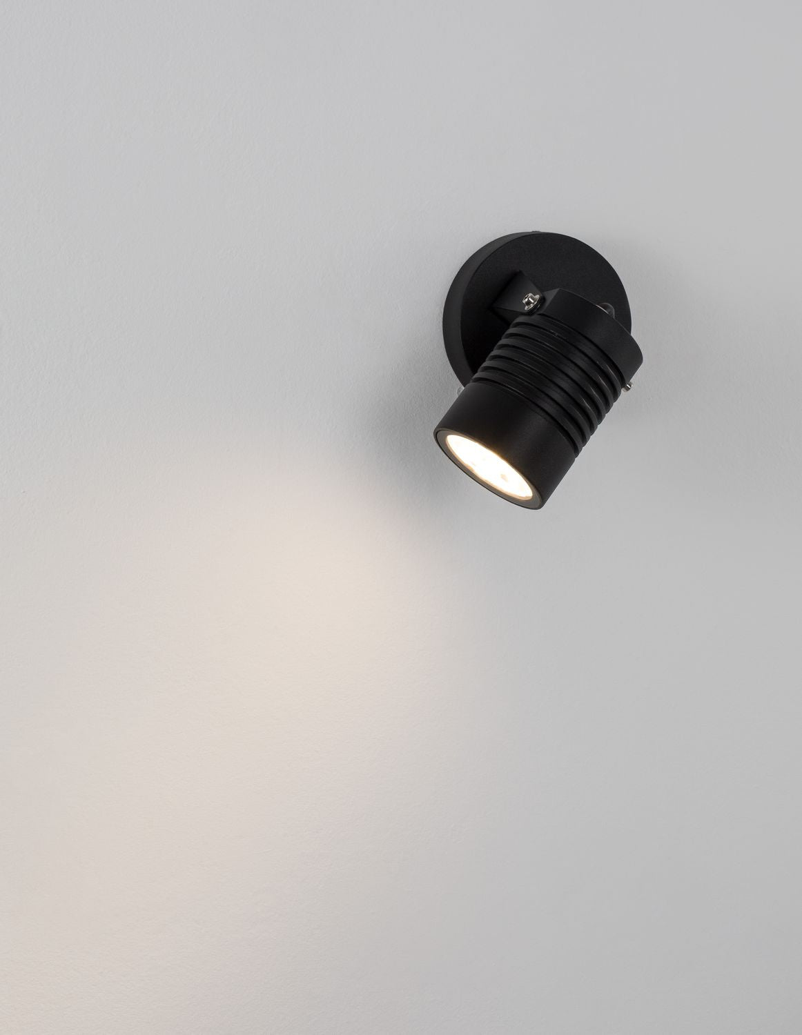 Applique allumée diffusant un halo lumineux chaud sur une paroi grise