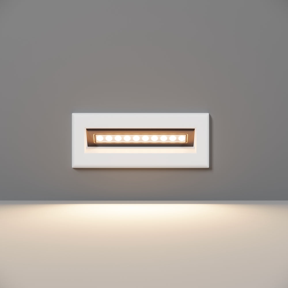 Luminaire mural encastré blanc rectangulaire allumé, vu de face sur mur gris