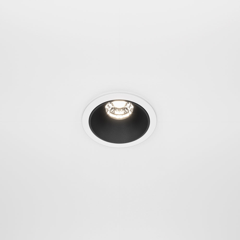 Spot encastré rond blanc vu de face dans un plafond, lumière allumée