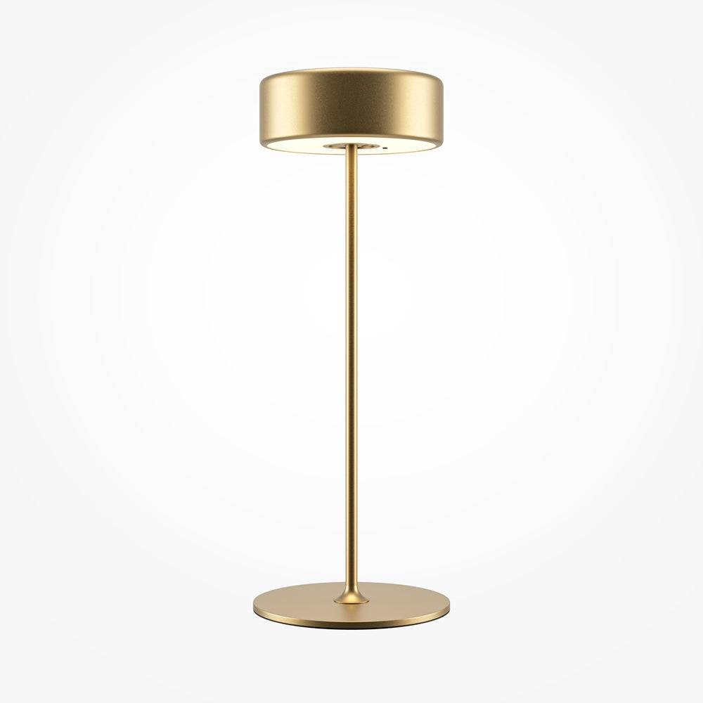 Lampe de table dorée de face sur fond blanc, abat-jour cylindrique et tige fine.