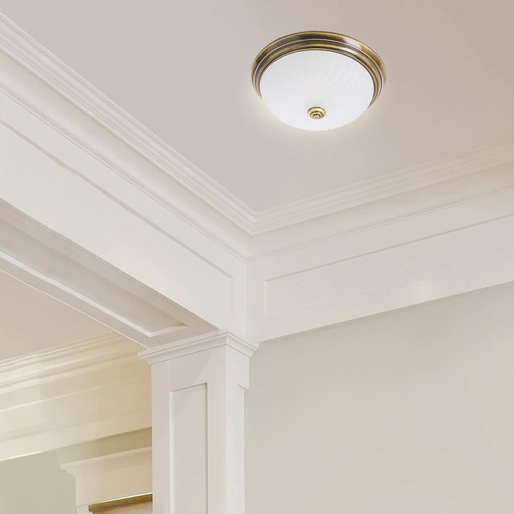 Luminaire fixé au plafond blanc avec corniche moulurée, éclairage doux allumé.