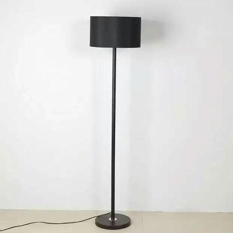 Lampadaire noir installé dans une pièce claire, câble d'alimentation visible au sol