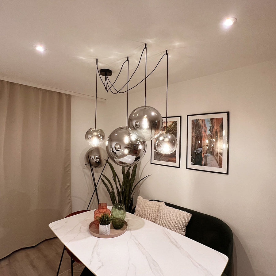 Suspension multiple à globes verre fumé et miroir, câbles noirs au-dessus d'une table.