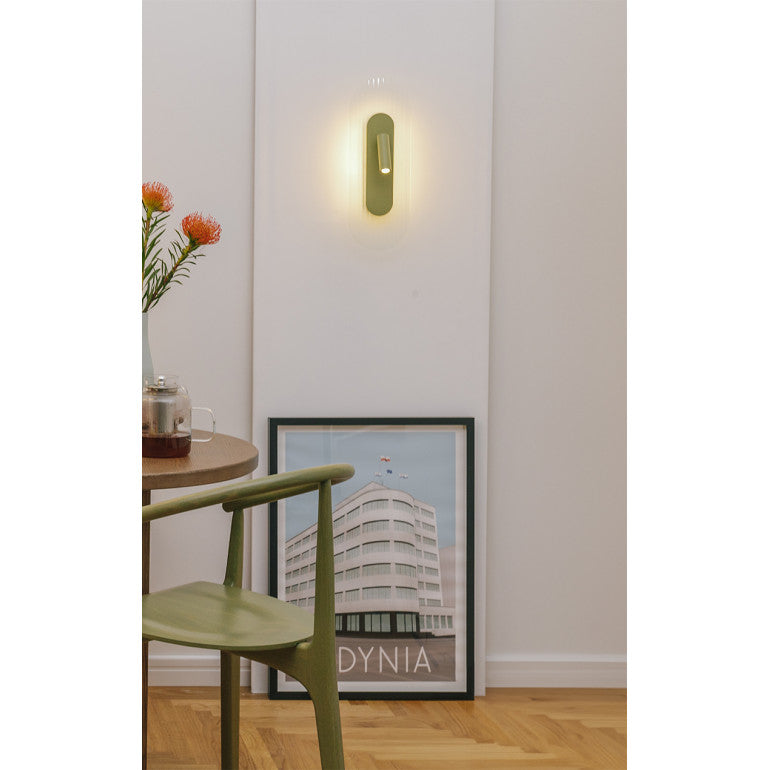 Mise en ambiance : applique verte allumée sur mur blanc, chaise et cadre