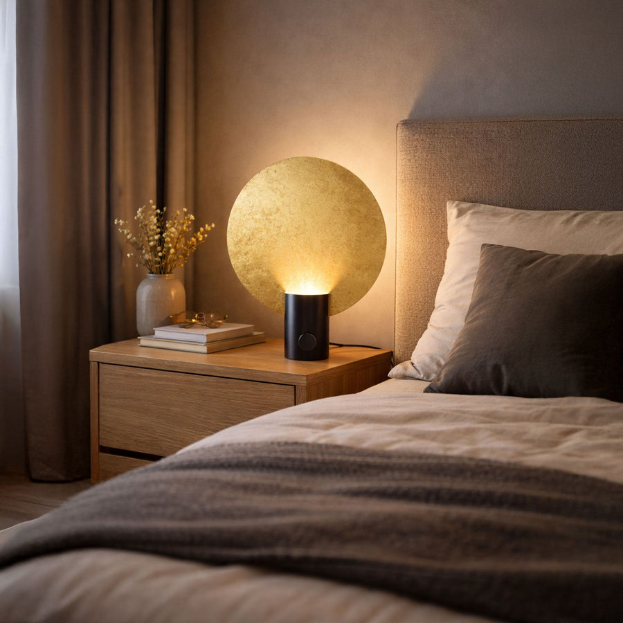 Lampe allumée au réflecteur doré posée sur une table de nuit en chambre.