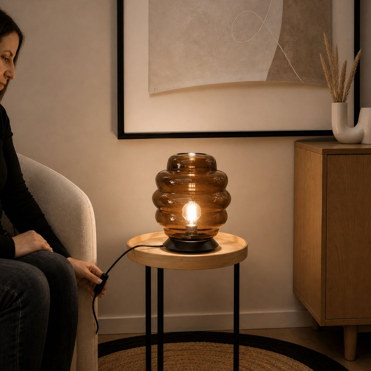 Lampe en verre ambré posée sur table ronde, femme assise à côté