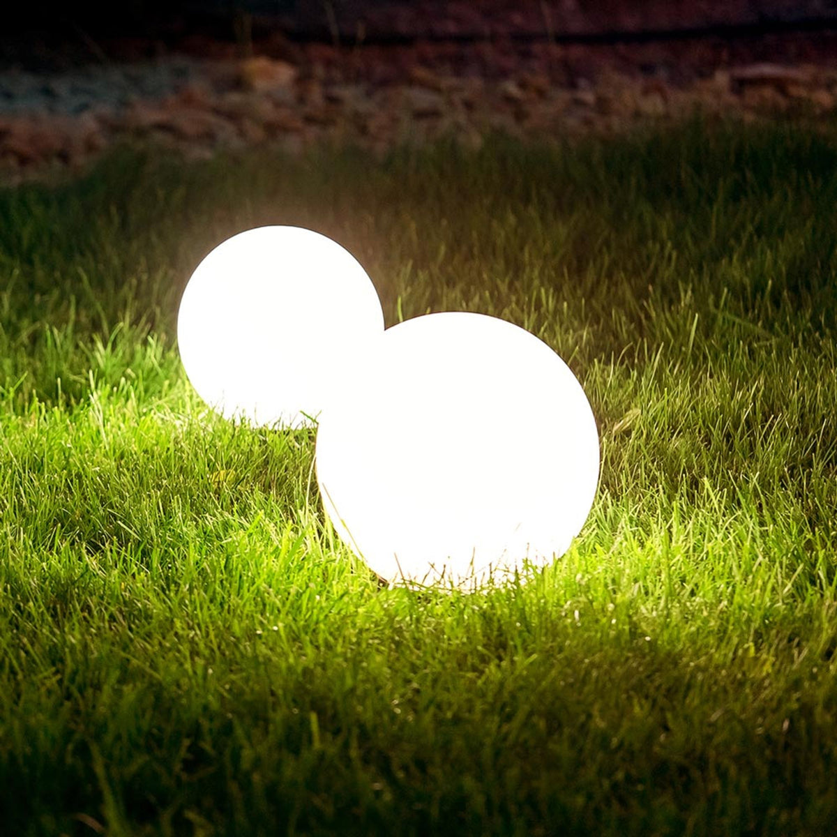Deux boules lumineuses blanches posées sur la pelouse éclairée, de nuit