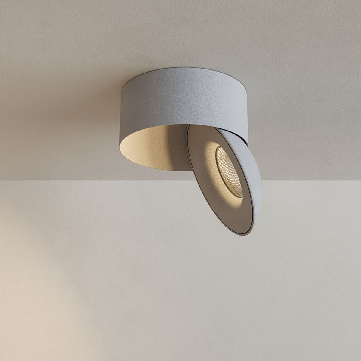 Vue de face d'un spot cylindrique blanc fixé au plafond, tête inclinée