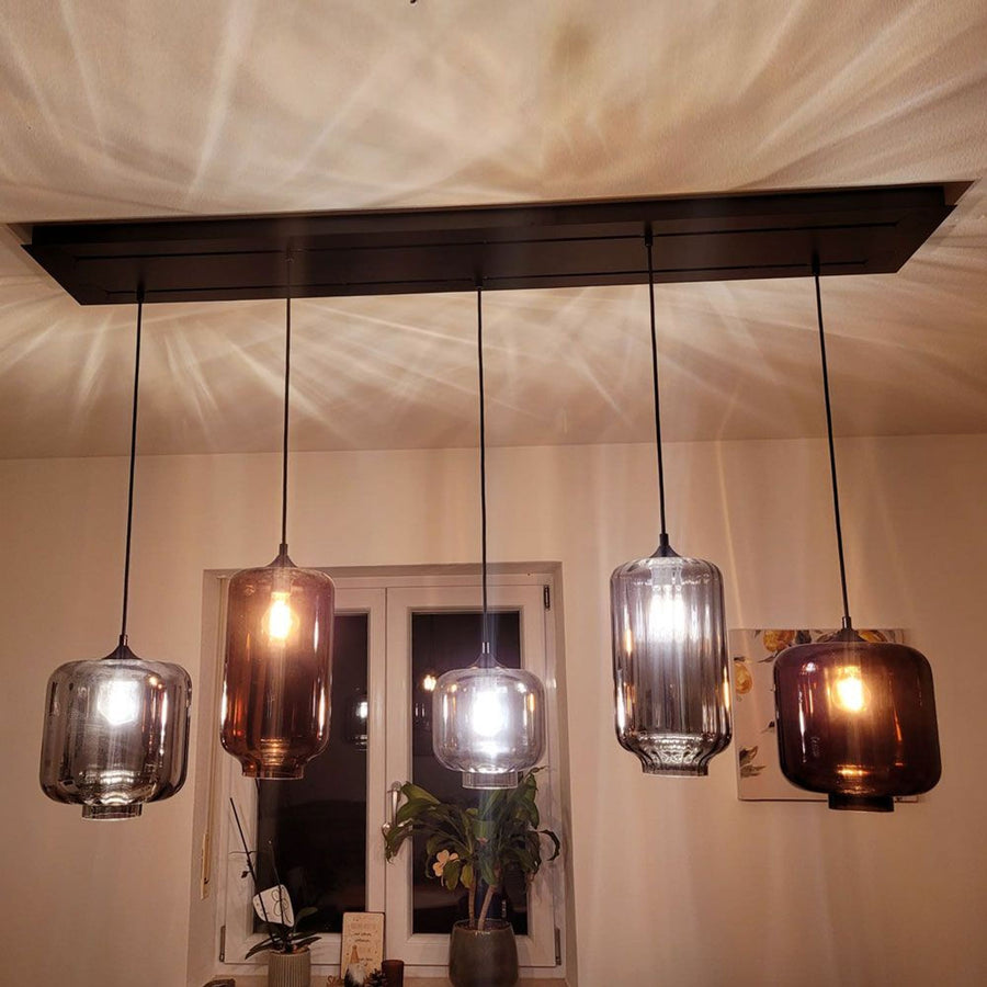 Cinq verres de formes variées suspendus devant une porte-fenêtre, ambiance chaleureuse du soir