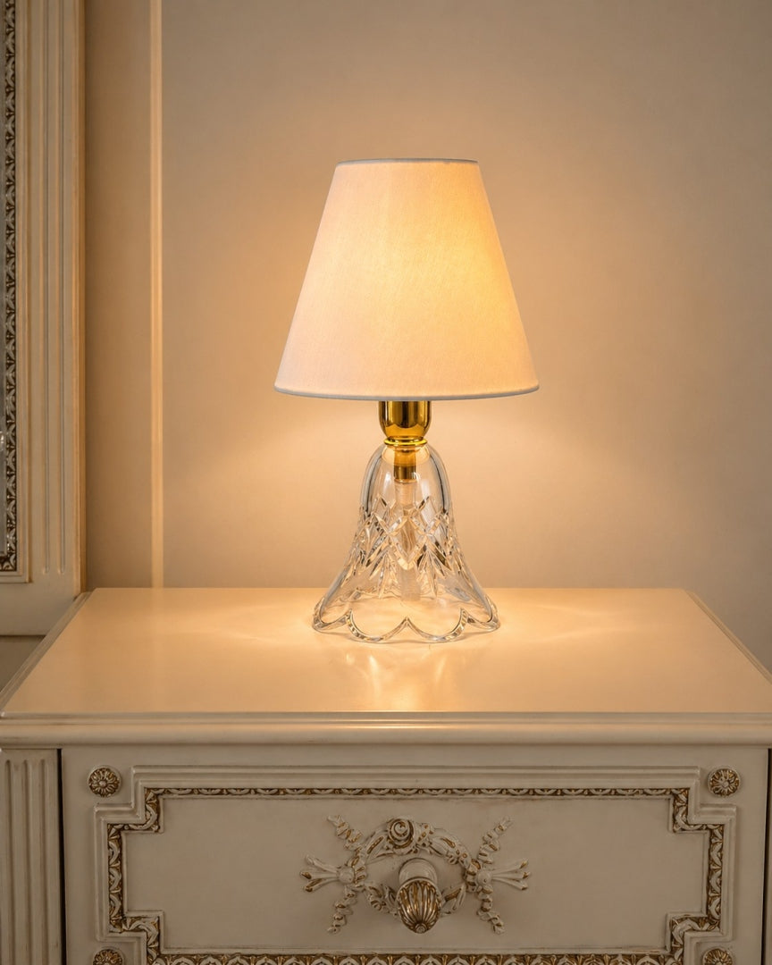 Lampe allumée sur une commode blanche moulurée, intérieur à l'ambiance dorée.