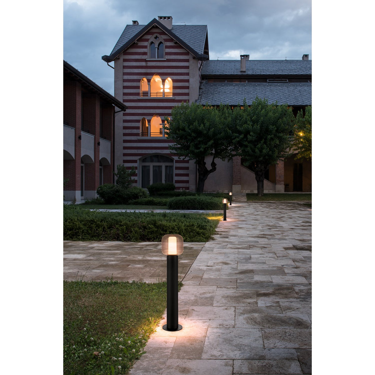Mise en ambiance nocturne : lampadaire éclairant une allée dallée devant un bâtiment.