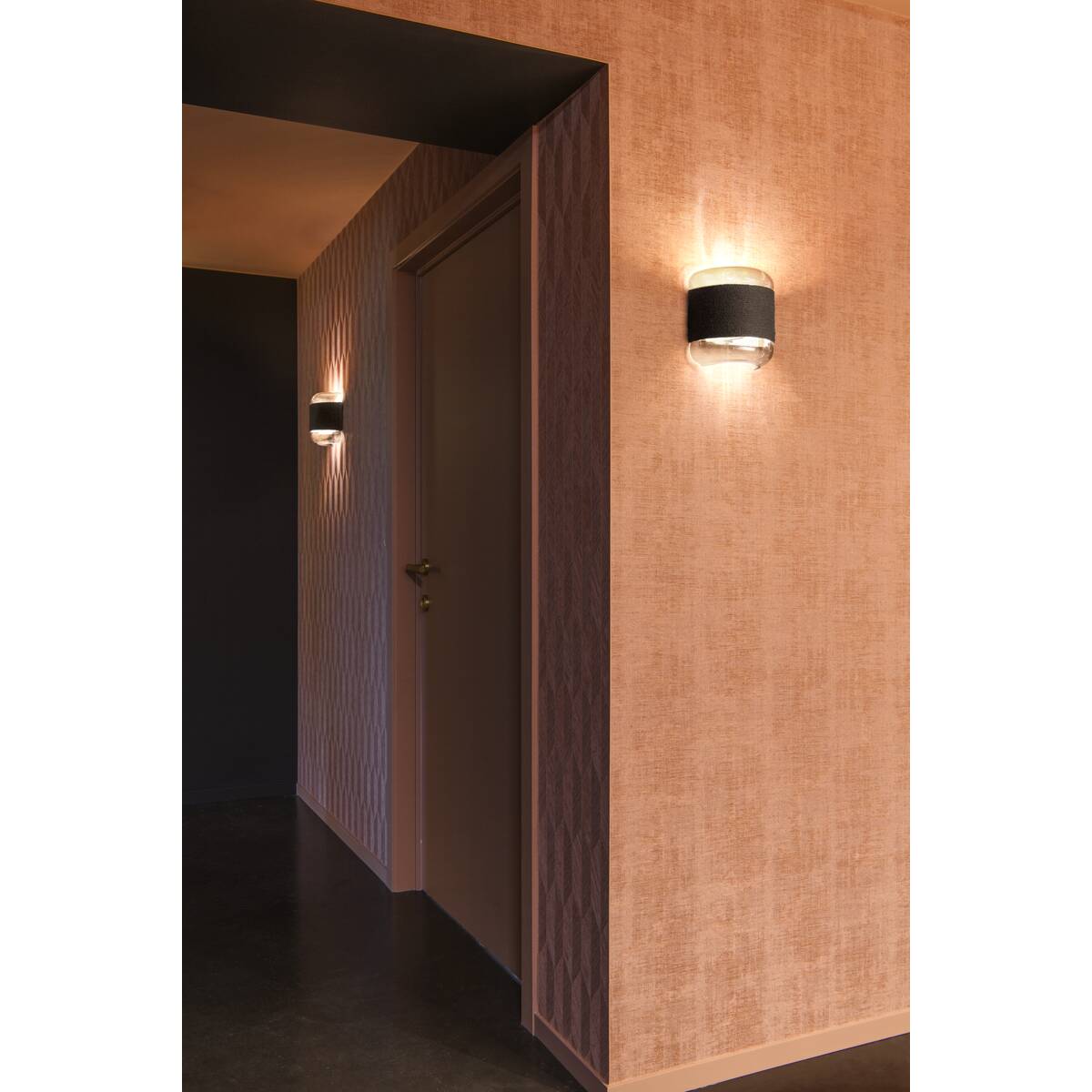 Couloir sombre éclairé par deux appliques murales projetant une lumière orangée sur les murs