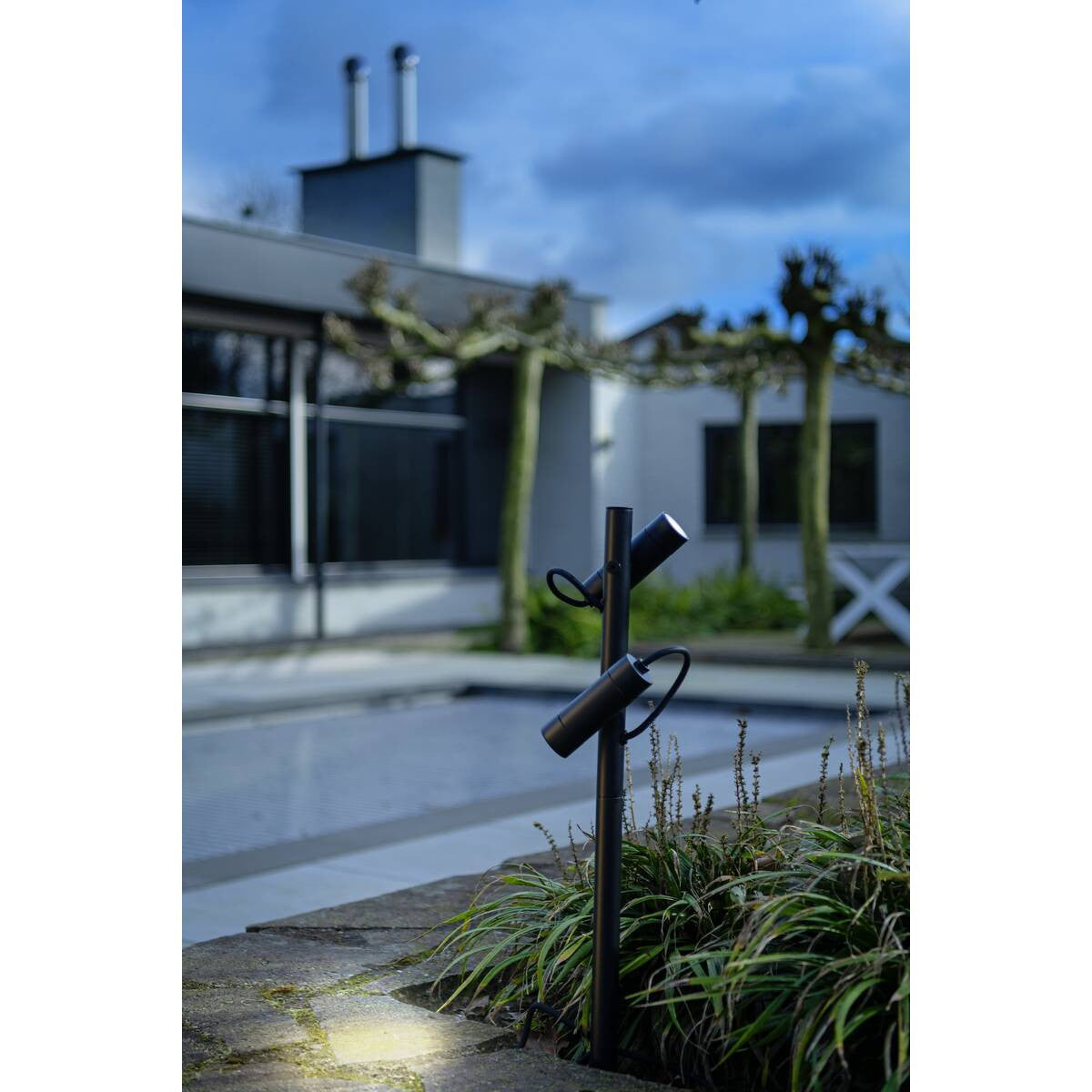Vue rapprochée du lampadaire planté dans les plantes, éclairant le sol devant une maison.