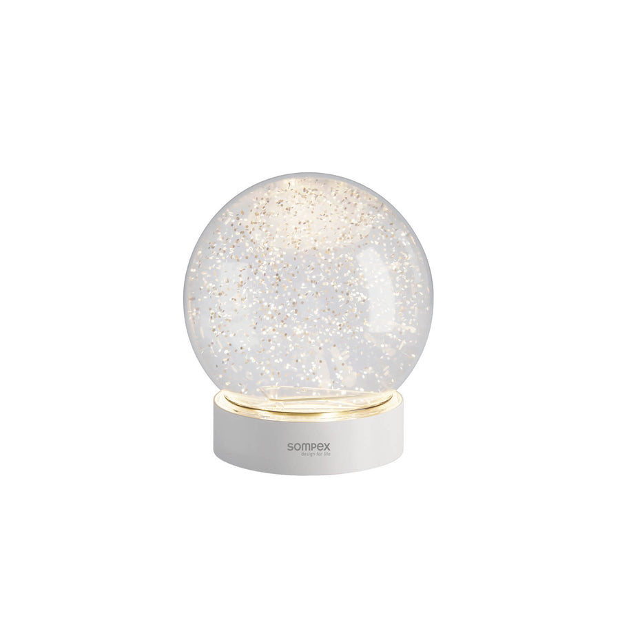 Lampe boule en verre transparent remplie de paillettes dorées sur socle blanc