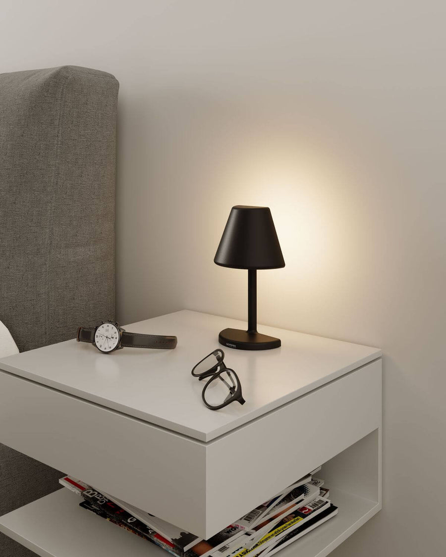Lampe posée sur une table de nuit blanche, près d'une montre et de lunettes.