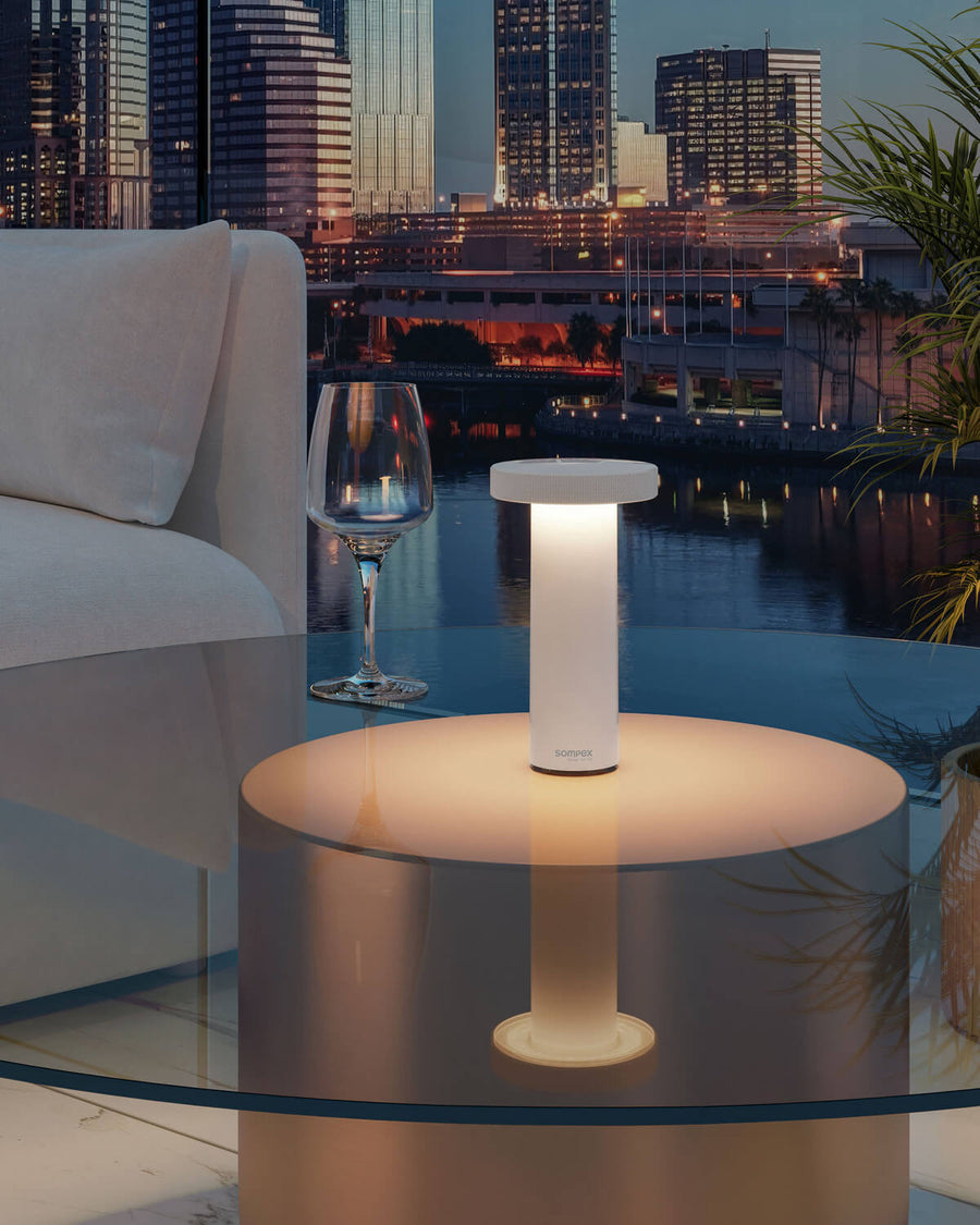 Lampe blanche allumée posée sur table en verre, terrasse urbaine au crépuscule