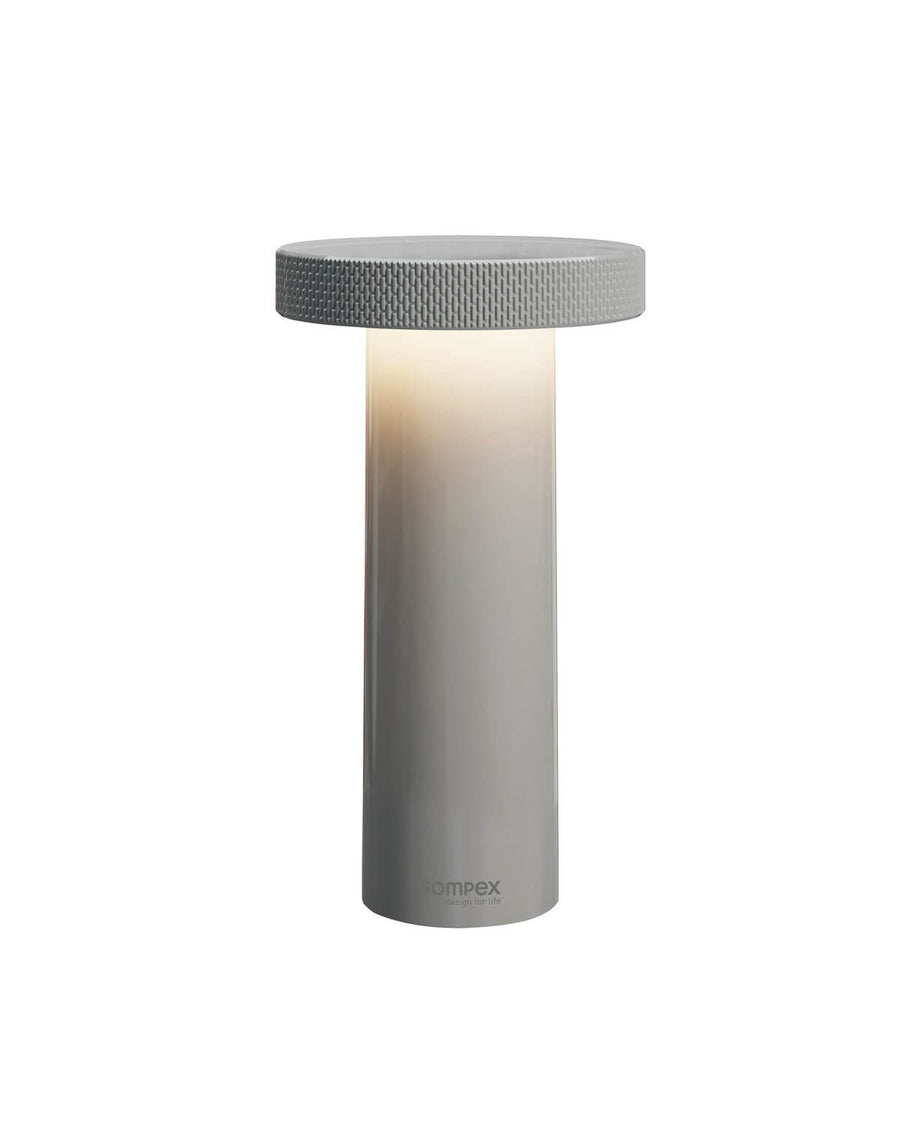 Lampe cylindrique grise de face sur fond blanc, sommet strié et lumière chaude.