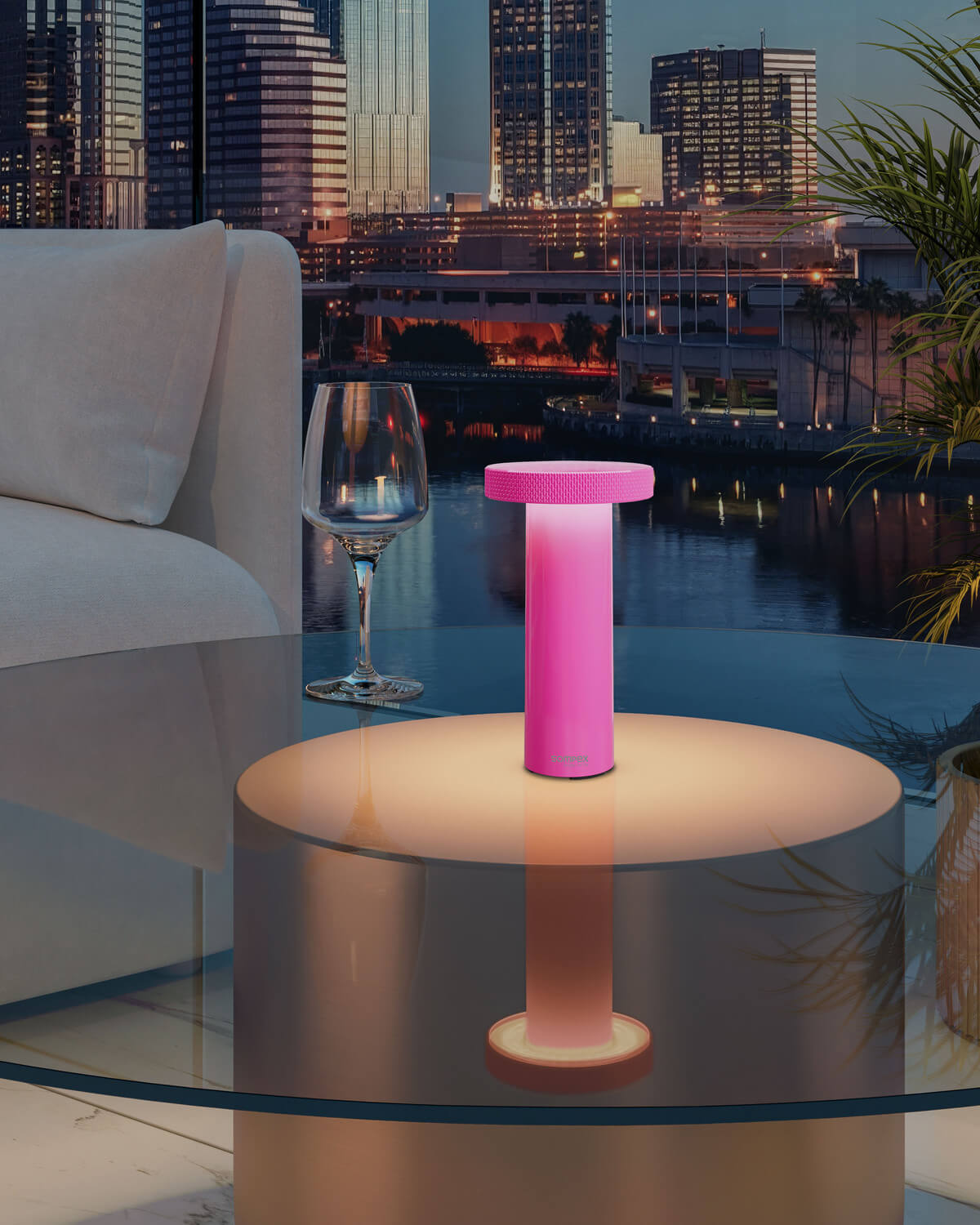 Lampe rose allumée posée sur table en verre, ambiance soirée urbaine avec gratte-ciel