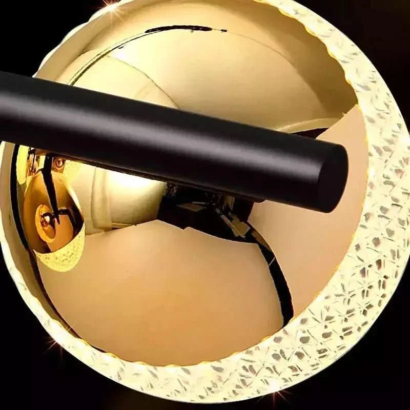 Détail du globe doré réfléchissant traversé par le tube horizontal noir mat.