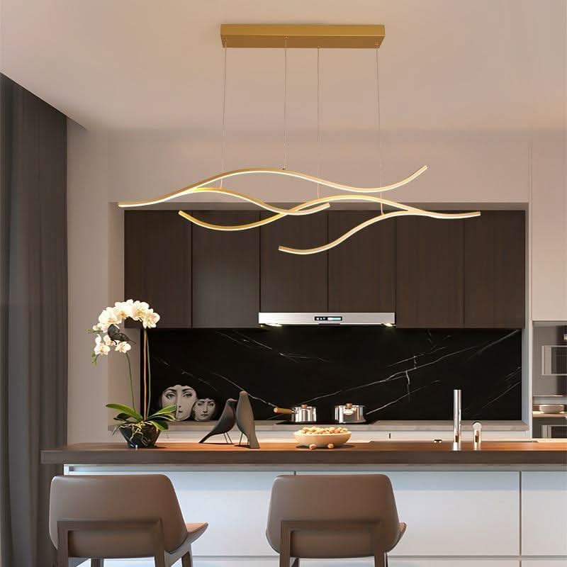 Luminaire laiton allumé au-dessus d'un îlot devant une crédence en marbre noir