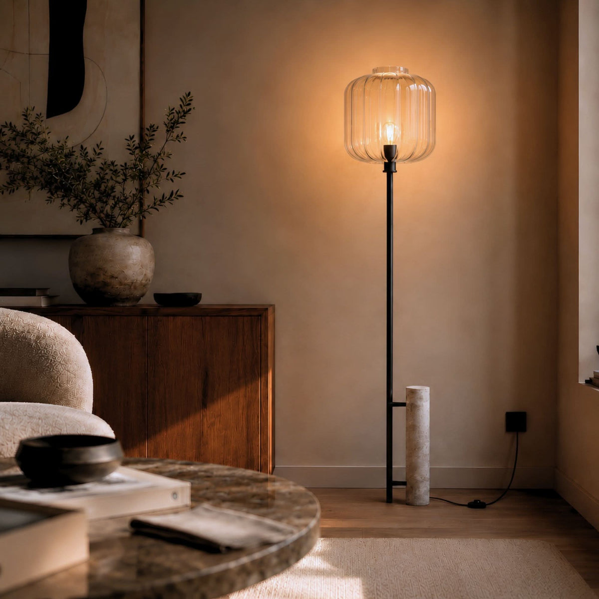 Lampadaire allumé dans un salon, verre transparent et socle en travertin posé au sol