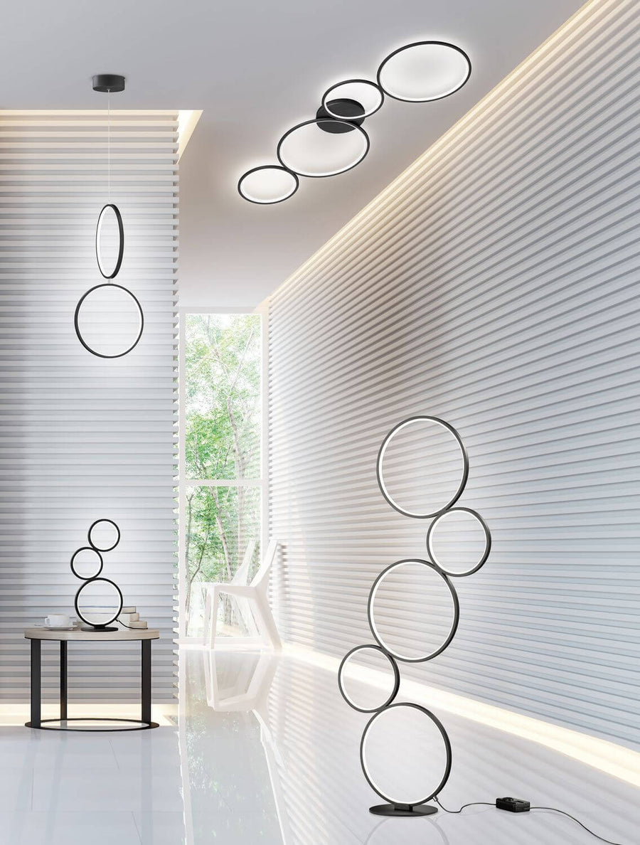 Mise en scène d'un salon avec lampadaire, suspension et plafonnier à anneaux noirs.