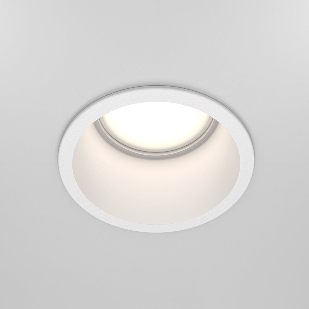 Vue de face d'un spot encastré blanc allumé dans un plafond gris.