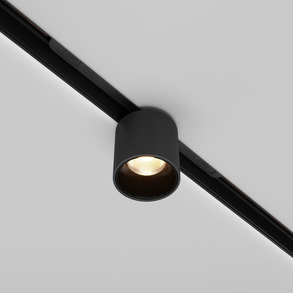 Spot cylindrique noir fixé sur rail, vu de trois quarts au plafond.