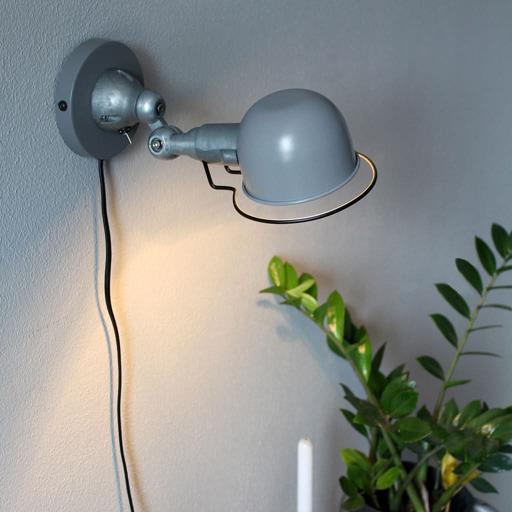 Applique allumée projetant une lumière chaude sur un mur gris, près d'une plante