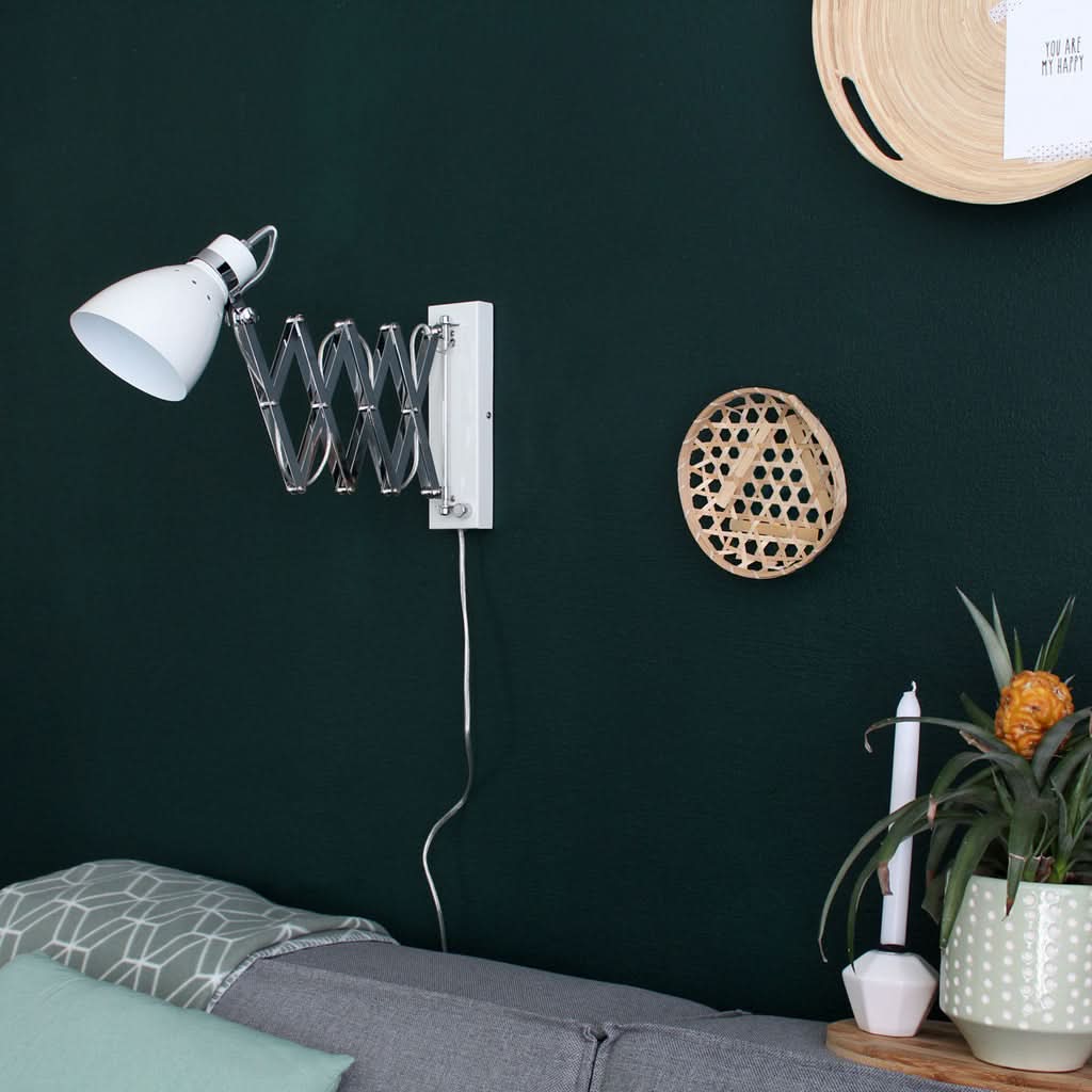 Applique orientable sur mur vert foncé dans un salon, câble visible.