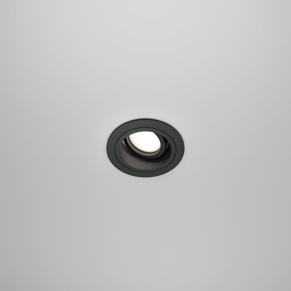 Vue de face d'un spot encastré rond noir dans un plafond blanc.