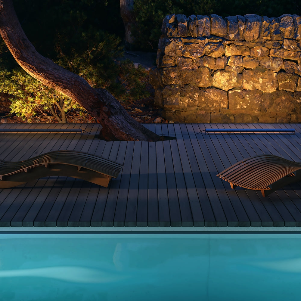 Mise en ambiance nocturne sur une terrasse en bois bordant une piscine.