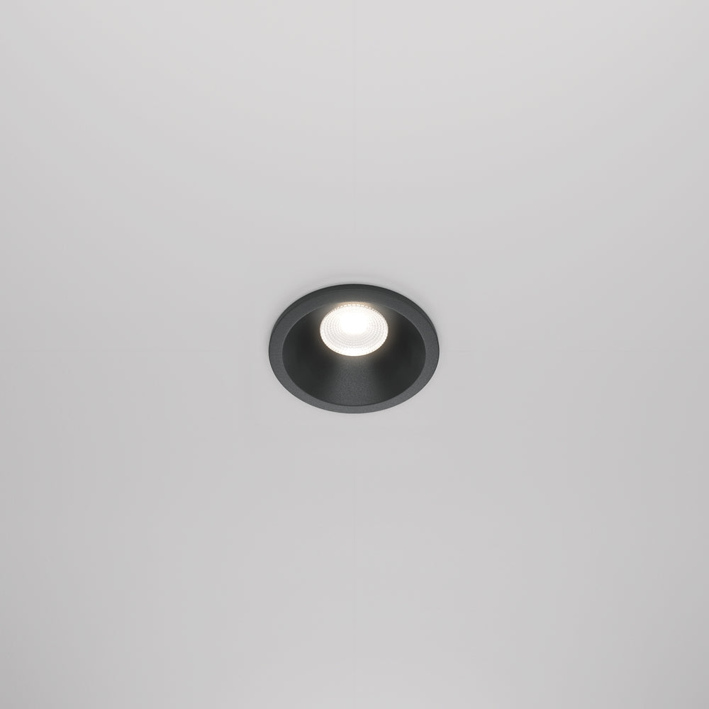 Spot encastré rond noir allumé, installé au plafond blanc, vue de face