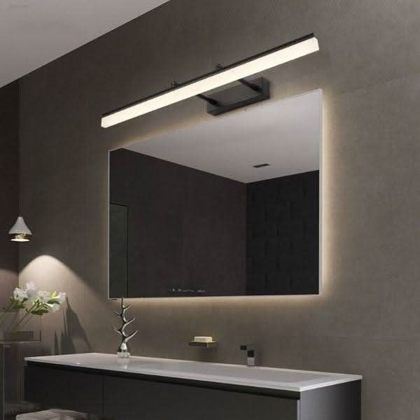 Vue d'ensemble d'une salle de bain sombre avec applique murale noire allumée au-dessus du miroir.