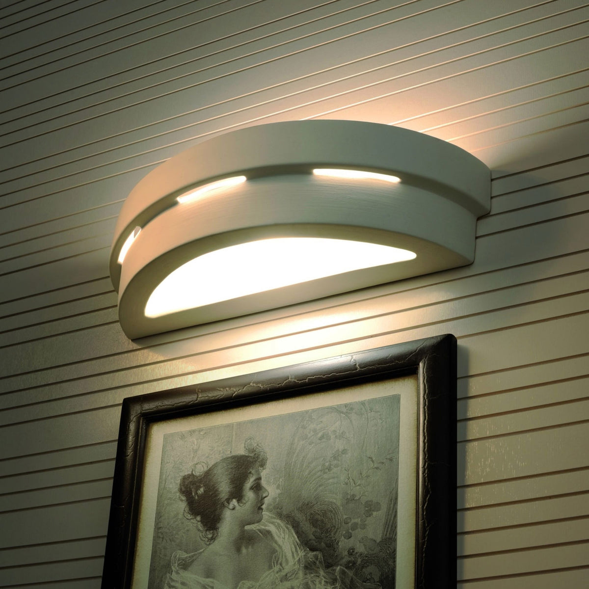 Mise en ambiance sur mur lambrisé, luminaire éclairant un tableau encadré