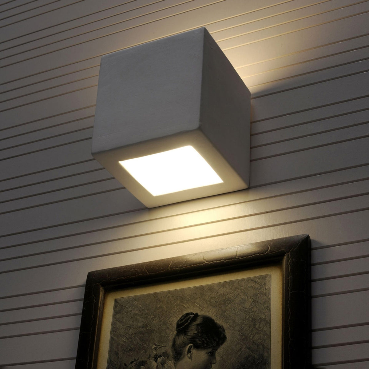 Applique cube blanc installée sous lambris, éclairant un tableau encadré de lumière chaude