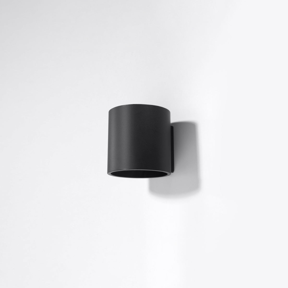 Vue de trois quarts d'une applique noire fixée sur un mur blanc, ombre portée visible.