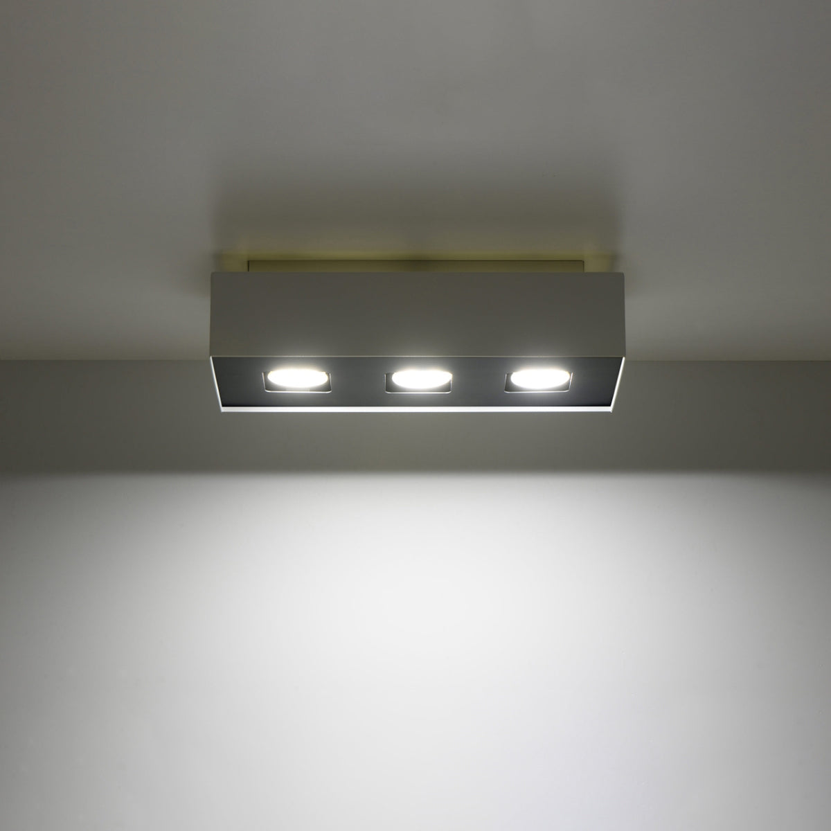 Luminaire allumé sous un plafond blanc, diffusant une lumière vive vers le bas
