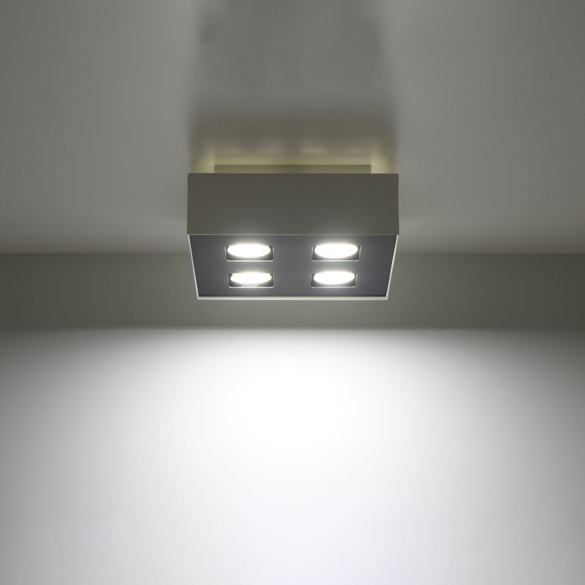 Plafonnier allumé au plafond diffusant un large halo lumineux blanc sur le mur