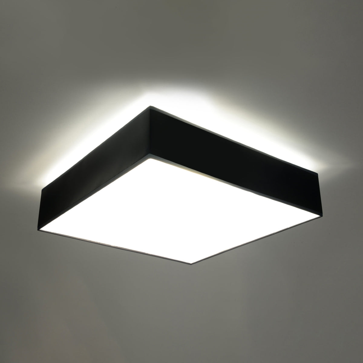 Plafonnier carré allumé, diffuseur blanc lumineux, halo de lumière sur le plafond.