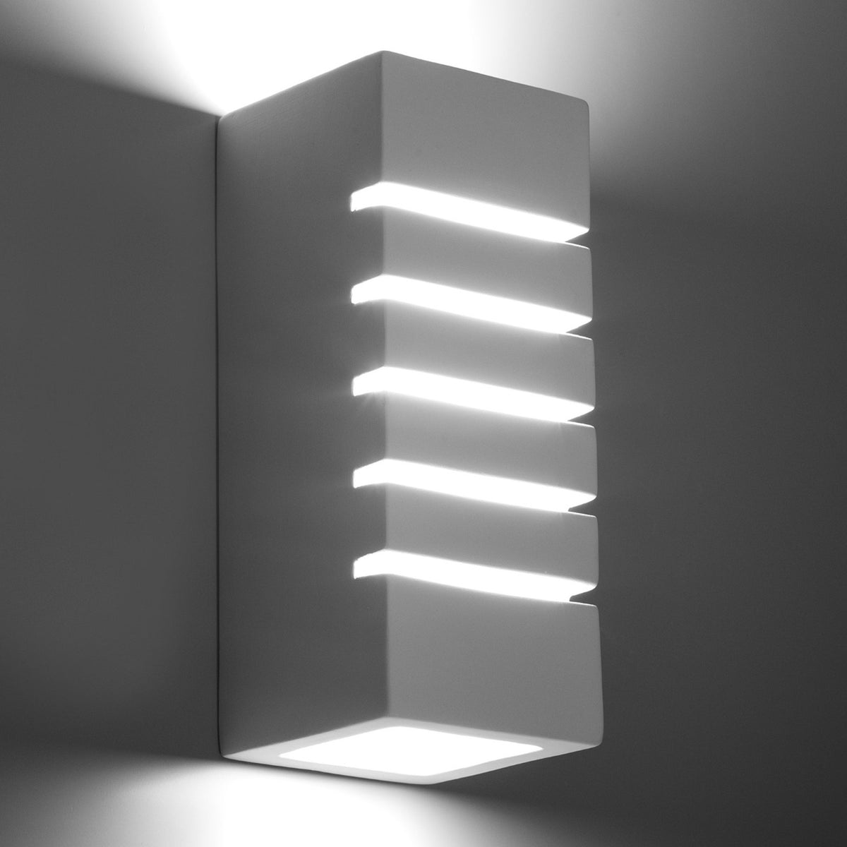 Vue rapprochée en lumière froide, applique murale blanche aux ouvertures lumineuses.