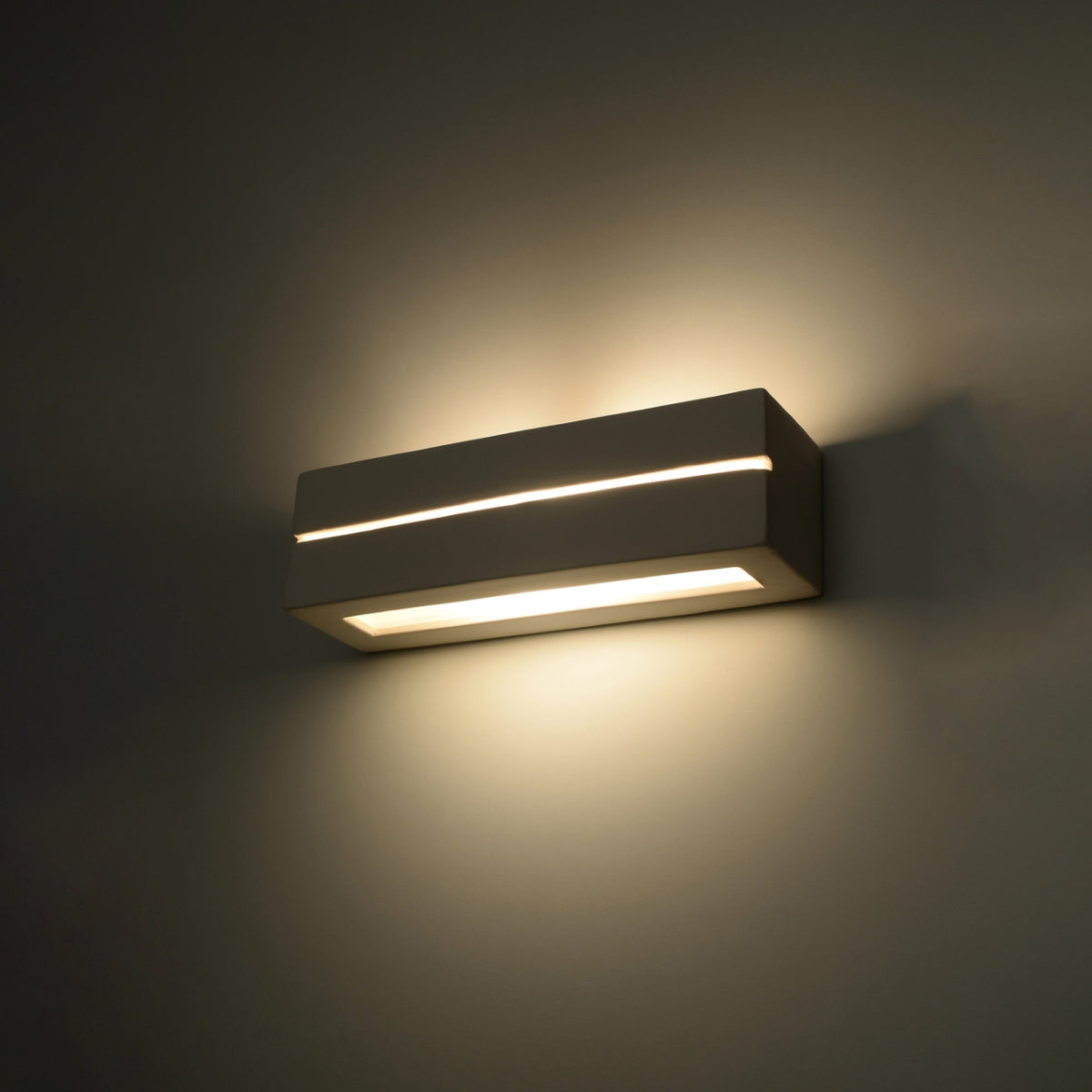Luminaire mural allumé dans une pièce sombre, lumière chaude projetée en haut et en bas.