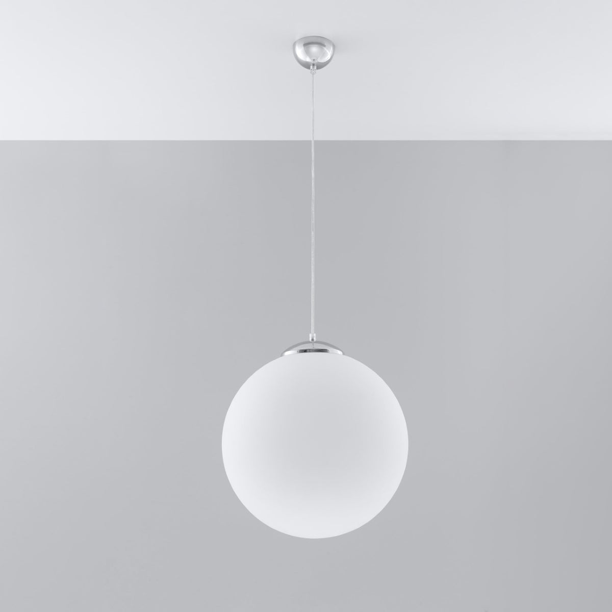 Suspension chromée installée sur un plafond, sphère blanche suspendue devant un mur gris.