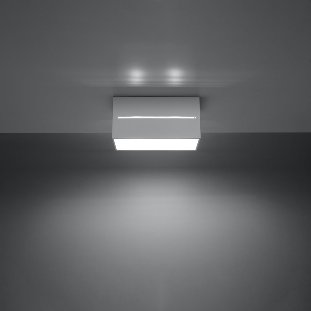 Vue de face du luminaire allumé, éclairant le plafond et diffusant une lumière blanche.