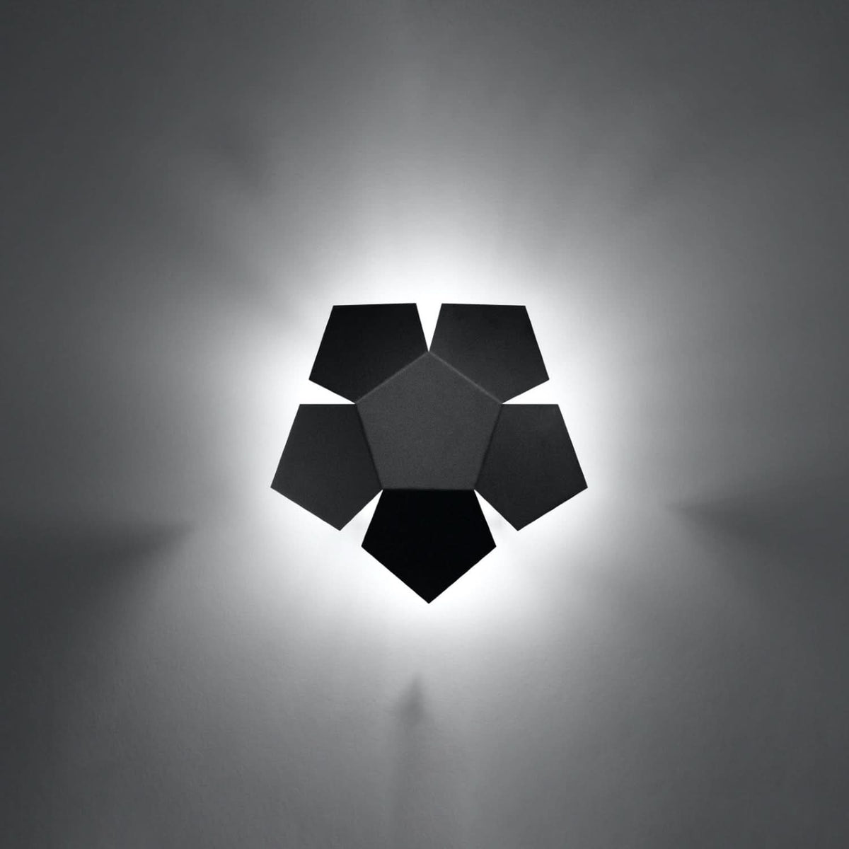 Applique allumée sur un mur, halo de lumière diffus autour des pentagones noirs