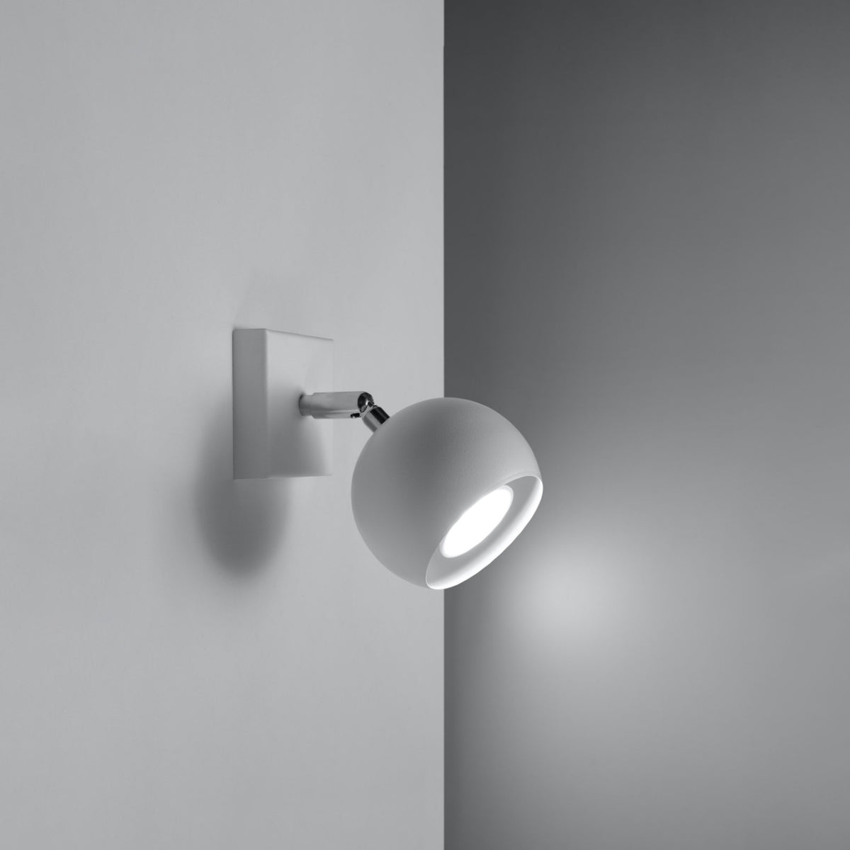 Applique allumée sur mur gris, orientée vers le bas, halo lumineux diffus