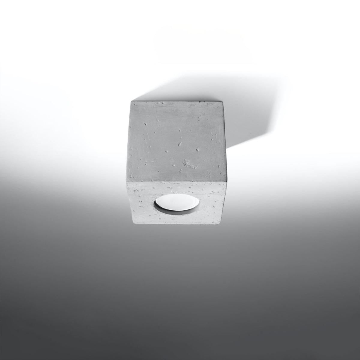 Vue de trois quarts du plafonnier cubique en béton sur fond gris clair.