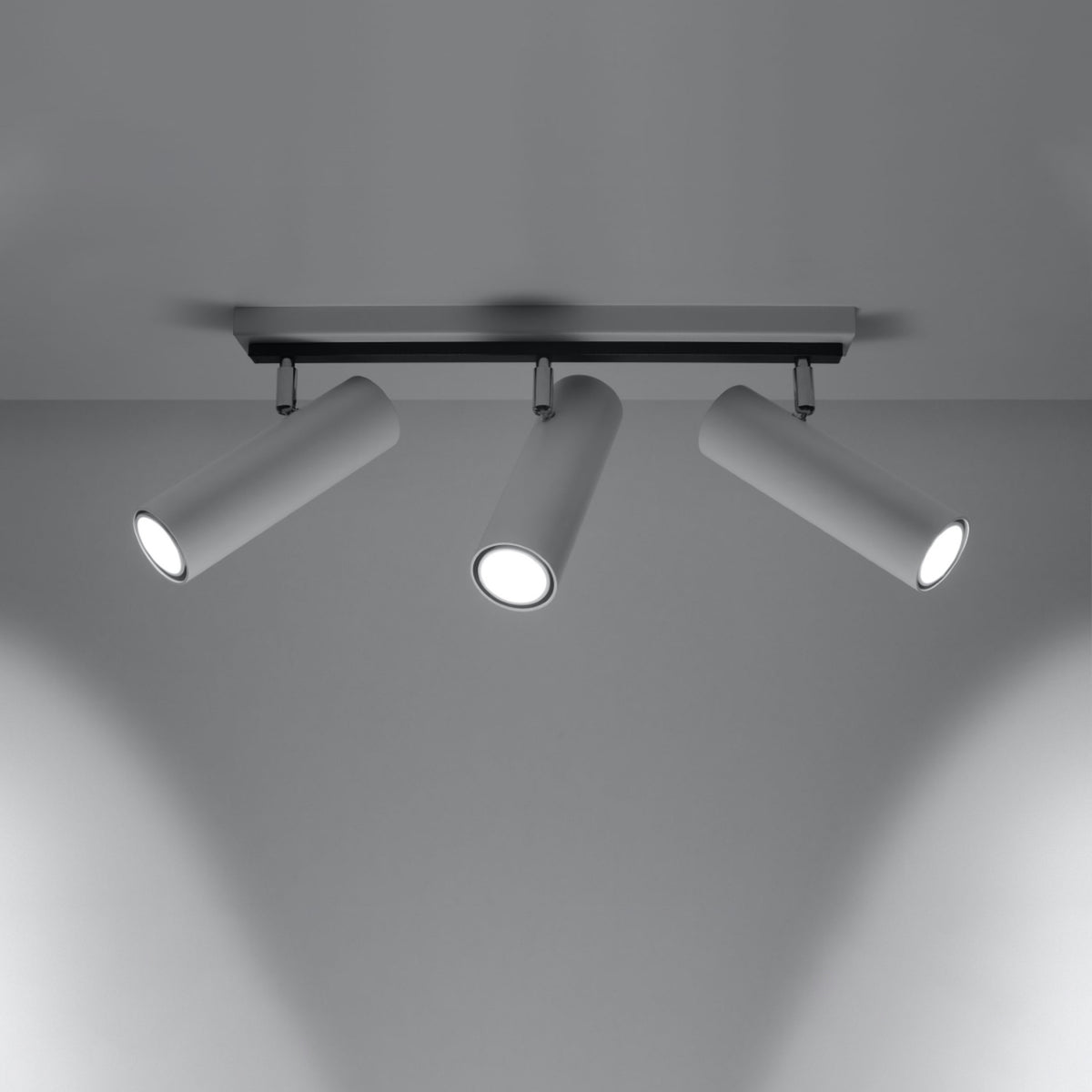 Luminaire allumé projetant trois faisceaux lumineux sur un mur gris.