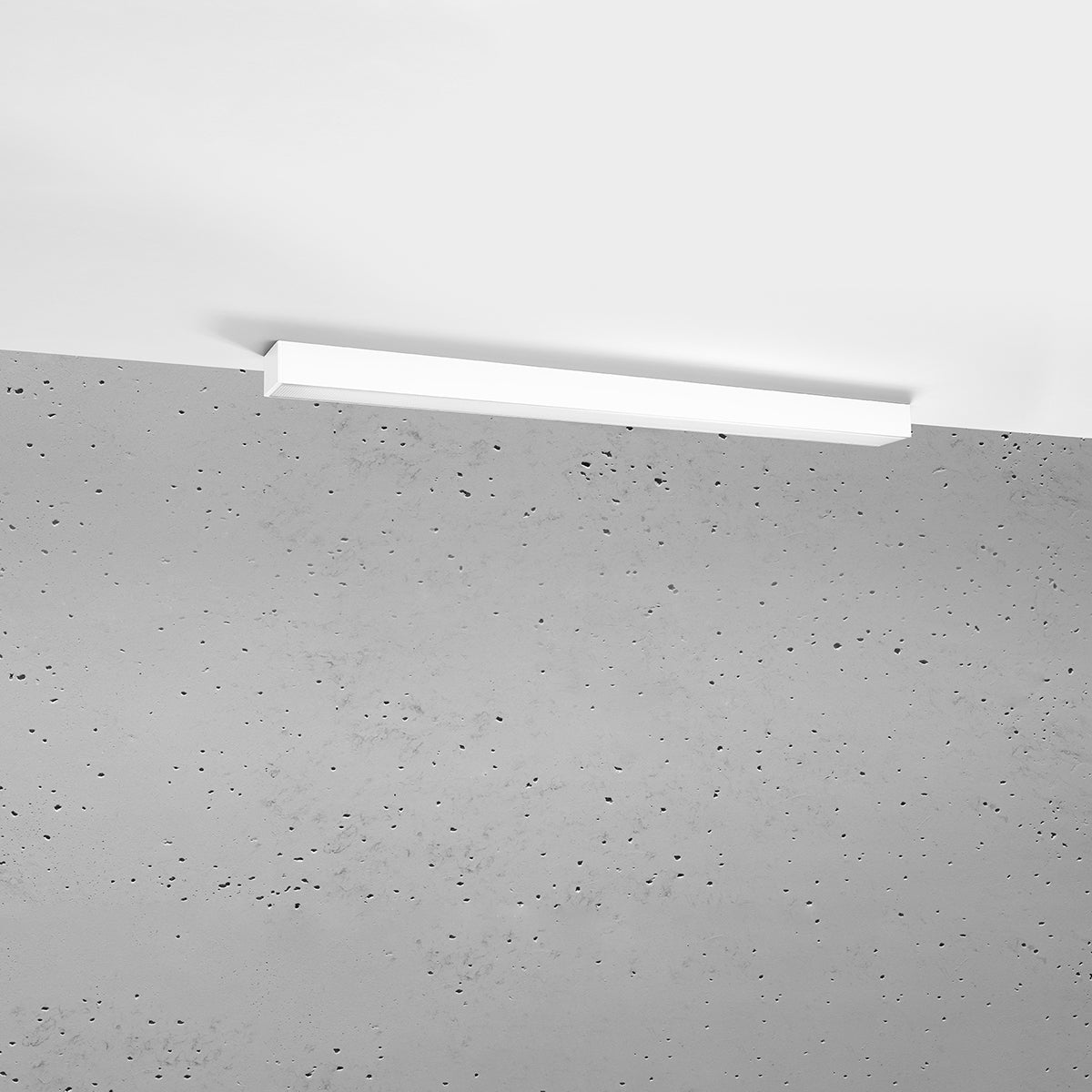 Plafonnier blanc fixé au plafond devant un mur en béton brut.