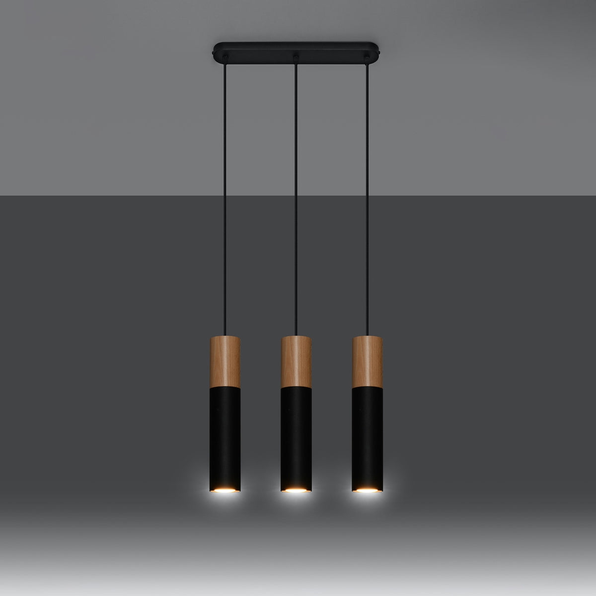 Même luminaire allumé, halo chaud sous chaque cylindre, ambiance tamisée sur fond sombre